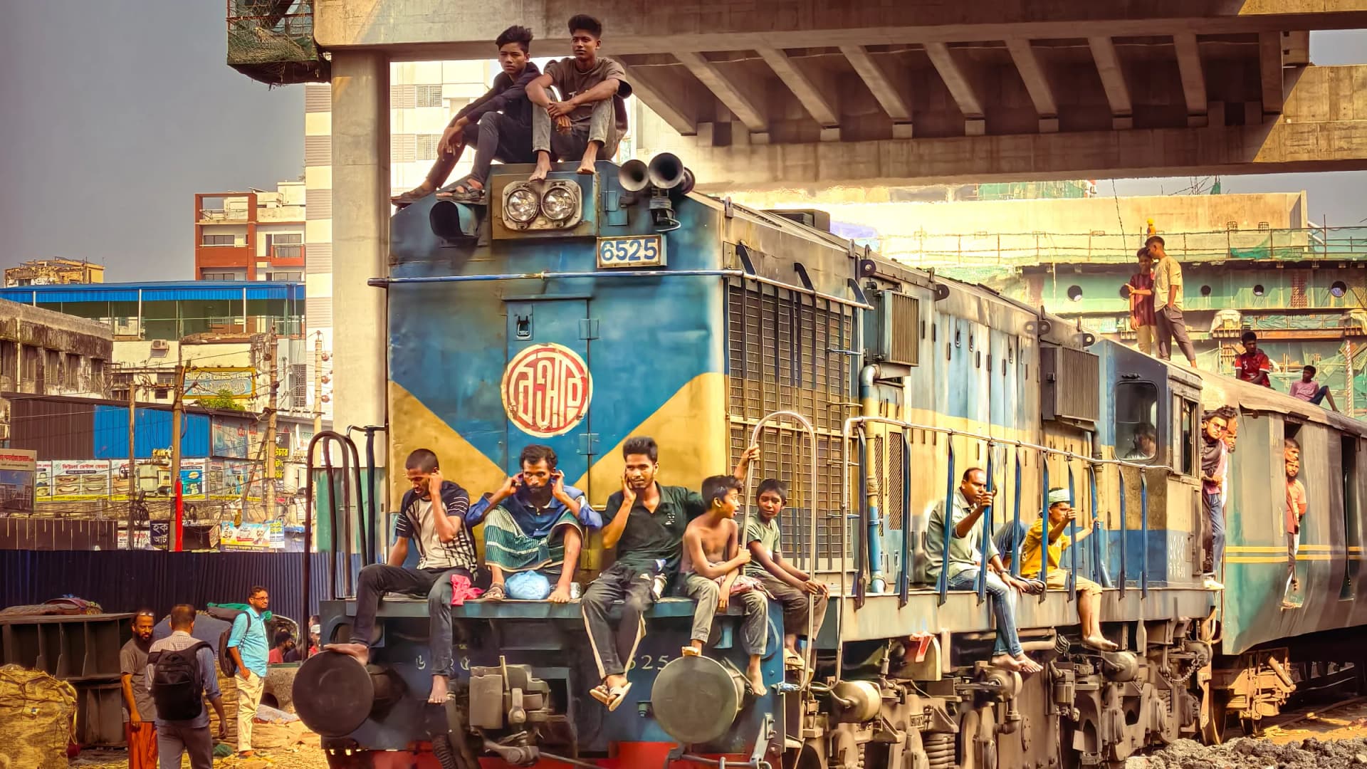 Passengers and commuters riding on a blue diesel locomotive under an elevated flyover