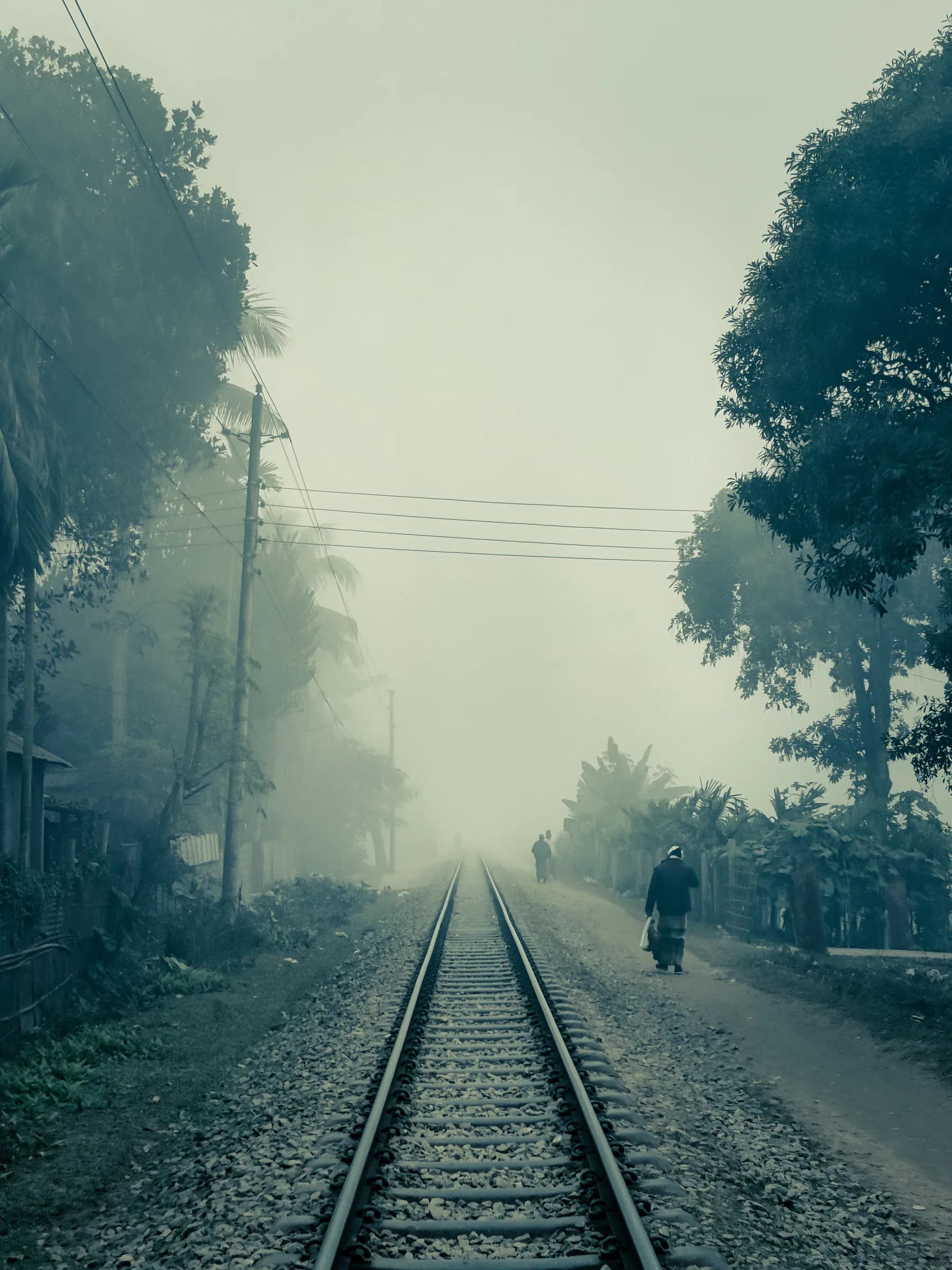 Single railway track disappearing into dense morning winter fog with walking pedestrians