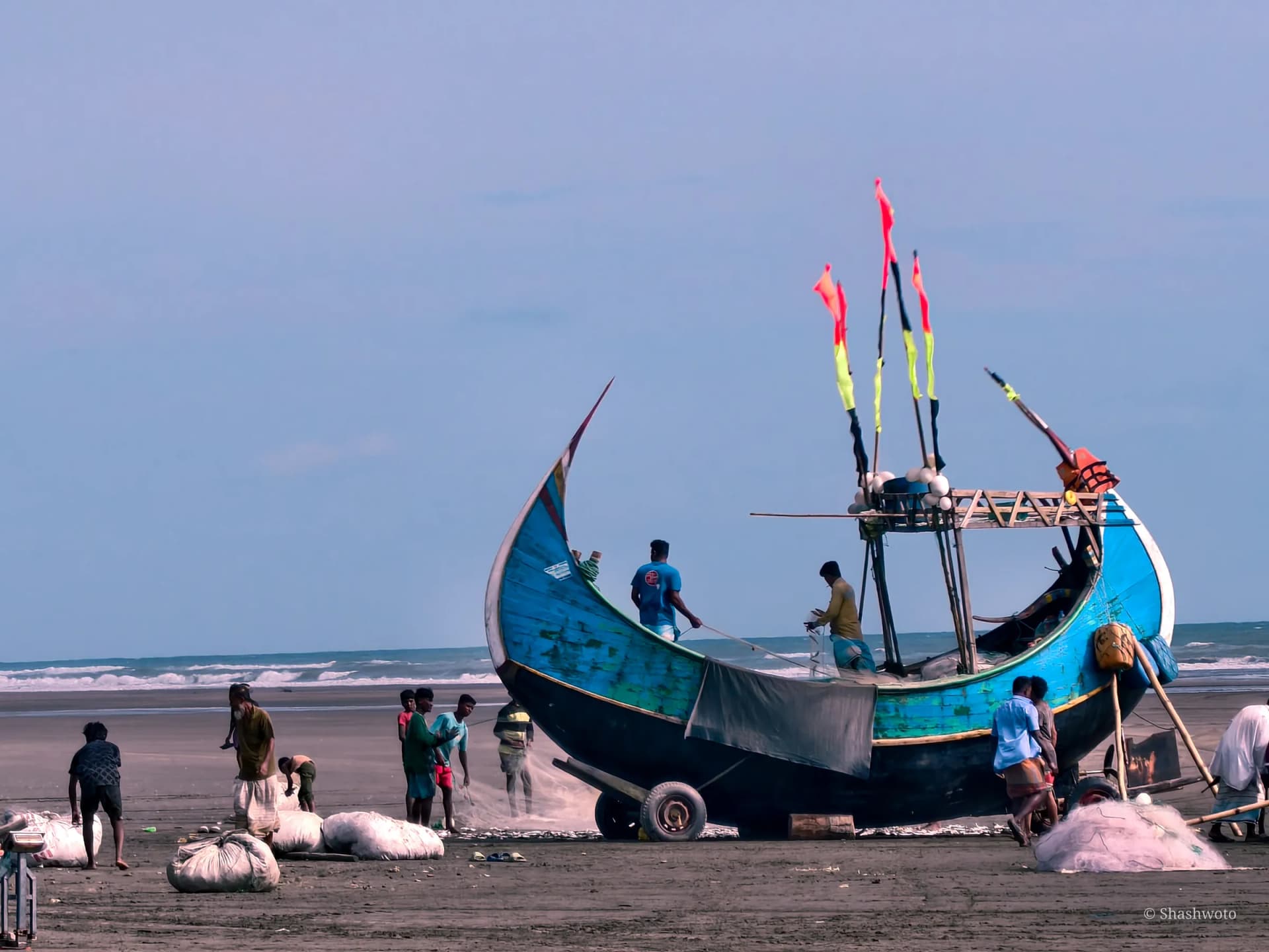 Crew working with fishing nets around a blue crescent boat on the beach
