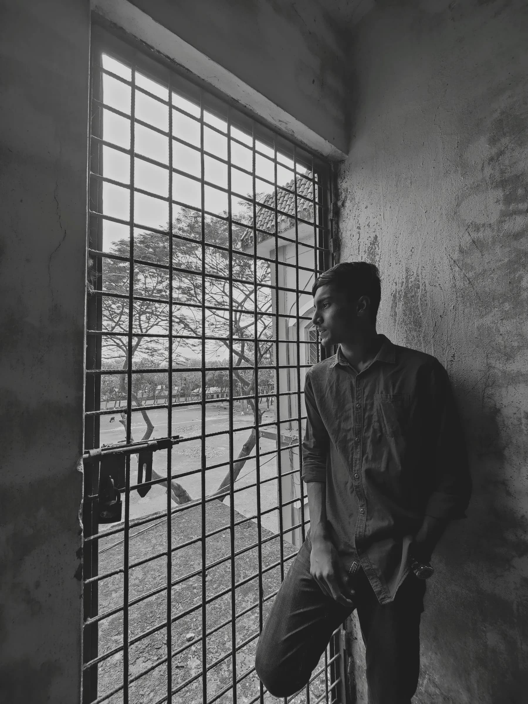 Mojaddid Shashwoto in profile looking through an iron window grille against a textured concrete wall
